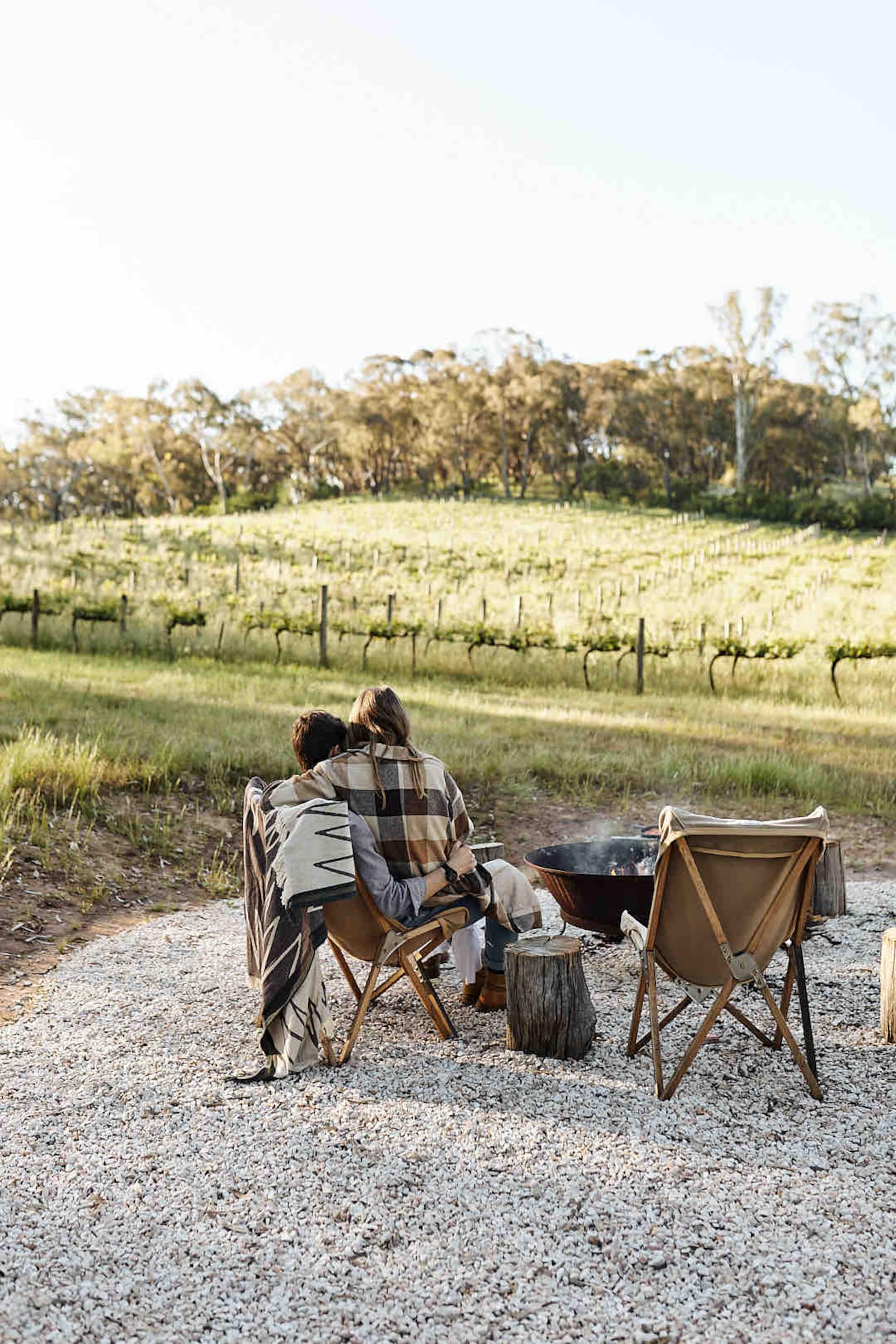 Two guests relaxing in camp chairs looking across the vines
